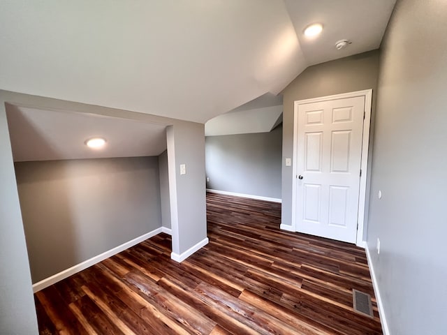 additional living space featuring visible vents, baseboards, lofted ceiling, and dark wood-style flooring