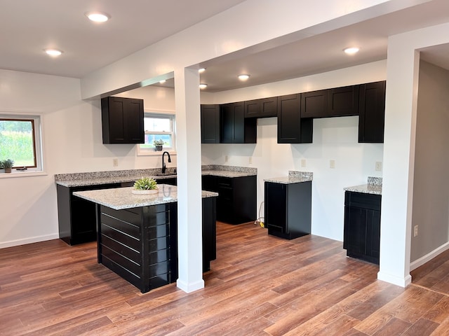 kitchen with a healthy amount of sunlight, a kitchen island, dark cabinetry, and wood finished floors