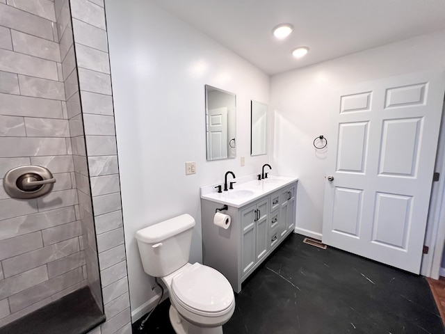 bathroom with baseboards, toilet, double vanity, tiled shower, and a sink