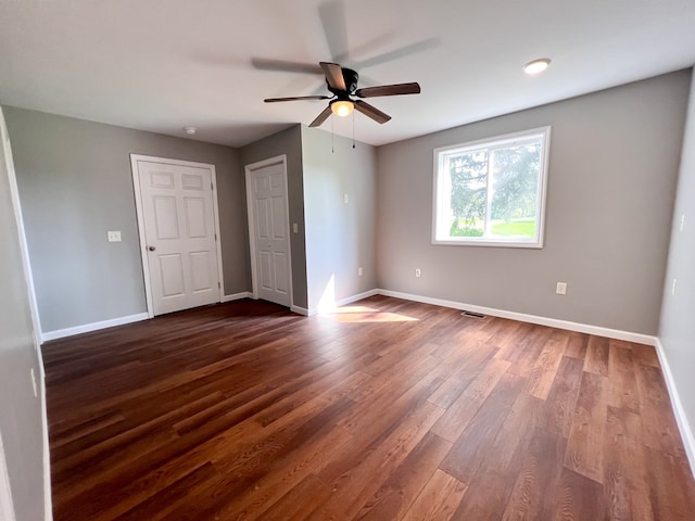 unfurnished bedroom featuring a ceiling fan, visible vents, dark wood-style floors, and baseboards