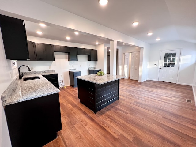 kitchen featuring light wood-style flooring, light stone counters, dark cabinets, and a sink