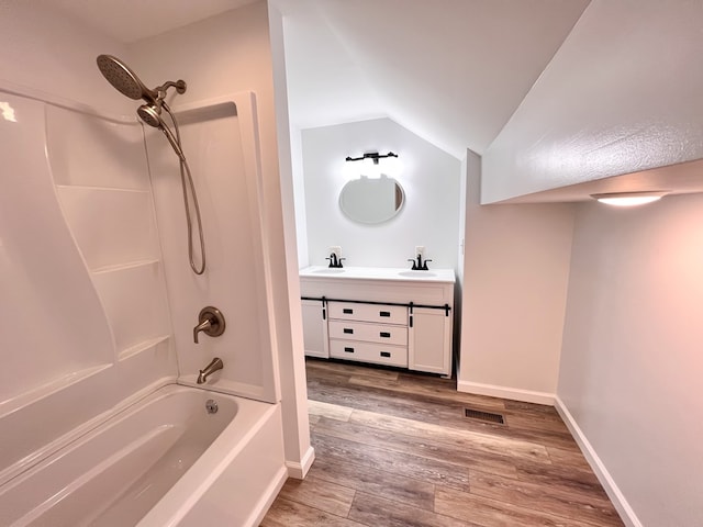 bathroom featuring wood finished floors, baseboards, shower / bath combination, lofted ceiling, and vanity