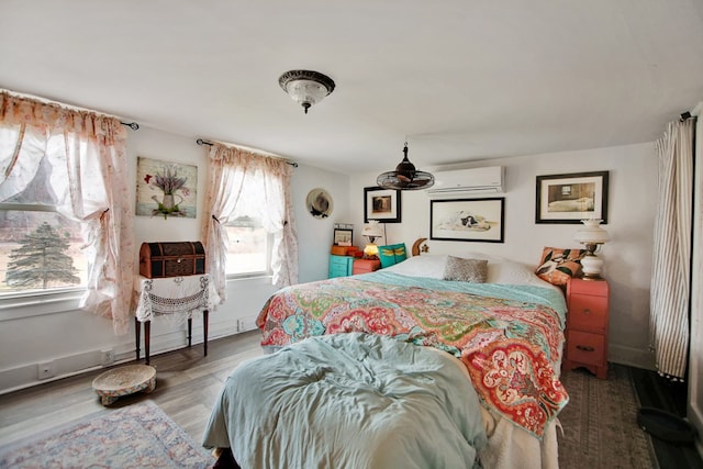 bedroom with an AC wall unit, baseboards, and wood finished floors