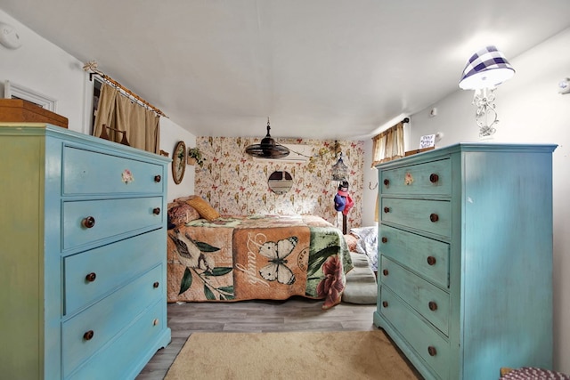 bedroom featuring an accent wall, wallpapered walls, and wood finished floors