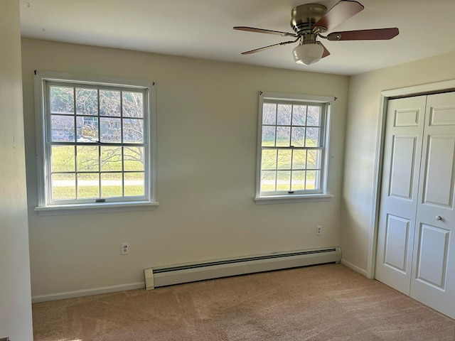 unfurnished bedroom featuring baseboard heating, multiple windows, ceiling fan, and light colored carpet