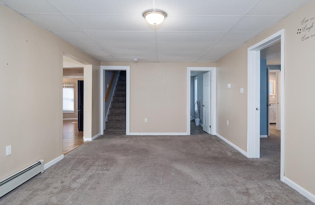 empty room with carpet floors, a baseboard radiator, and a paneled ceiling