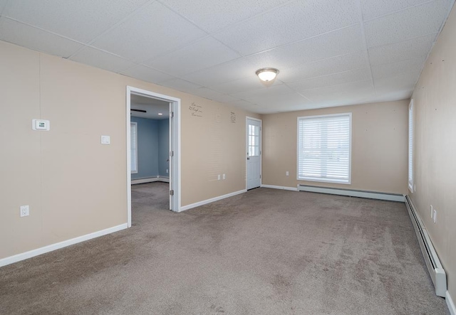 empty room with carpet flooring, a drop ceiling, and baseboard heating