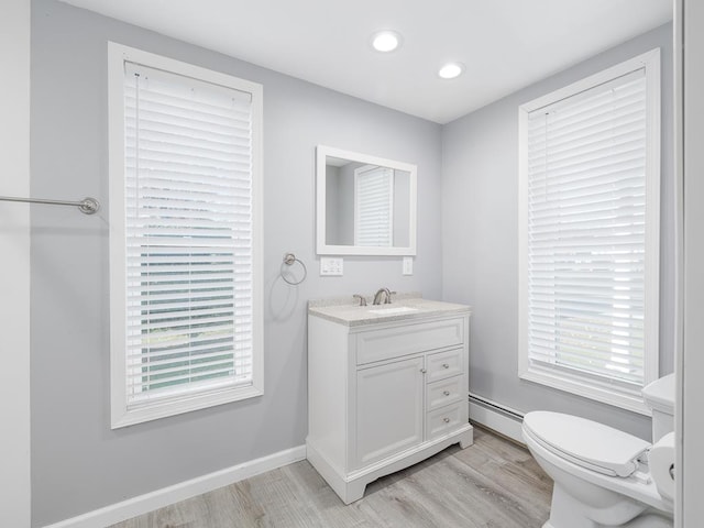 bathroom with toilet, vanity, a baseboard heating unit, and hardwood / wood-style flooring