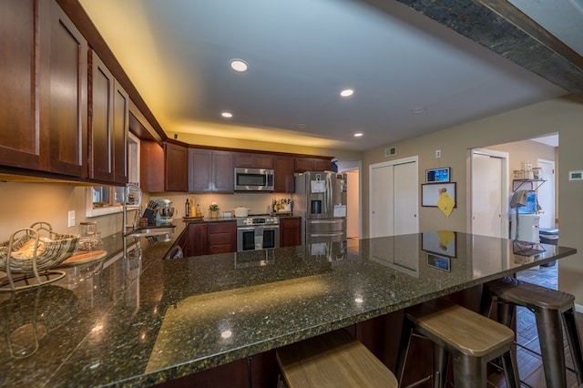 kitchen featuring a kitchen bar, sink, dark stone counters, and appliances with stainless steel finishes