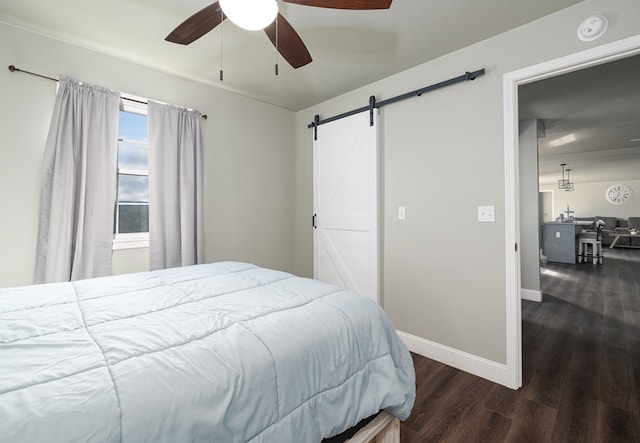 bedroom with ceiling fan, a barn door, and dark wood-type flooring