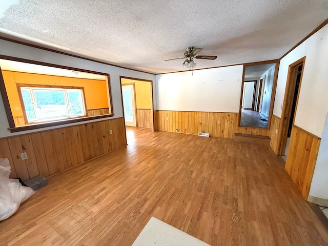 unfurnished living room featuring wood walls, ornamental molding, a textured ceiling, and light wood-type flooring