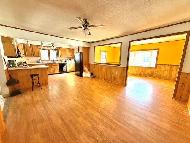 unfurnished living room featuring crown molding, wooden walls, a textured ceiling, and light wood-type flooring