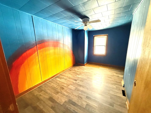 empty room featuring wood walls, ceiling fan, and light wood-type flooring