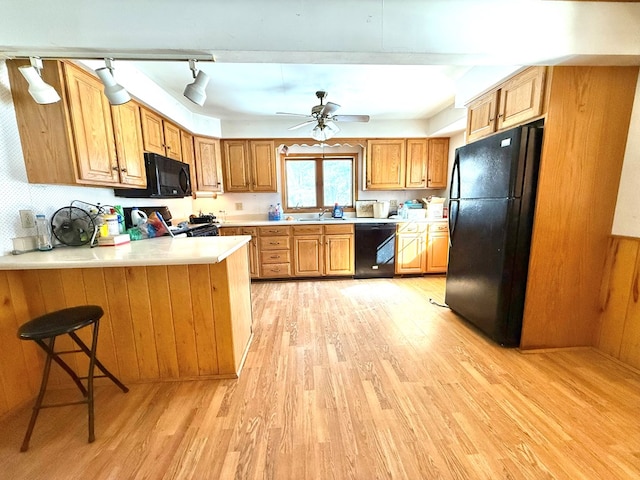 kitchen with a kitchen breakfast bar, kitchen peninsula, ceiling fan, light hardwood / wood-style floors, and black appliances