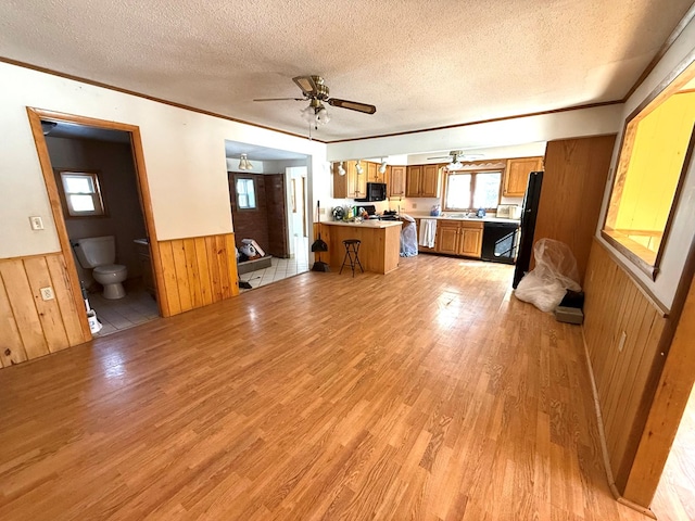 kitchen featuring wood walls, light hardwood / wood-style floors, kitchen peninsula, crown molding, and a textured ceiling