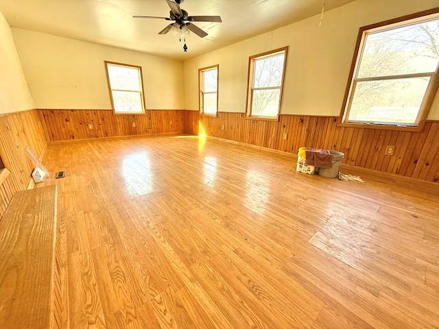 spare room with ceiling fan, wood walls, and light wood-type flooring