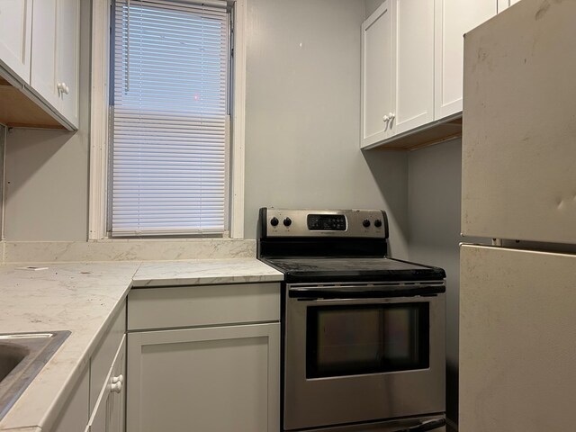 kitchen featuring white fridge, sink, stainless steel electric range, and white cabinets