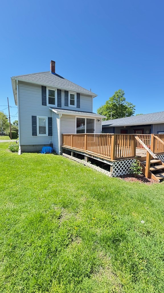 rear view of property featuring a chimney, a lawn, and a wooden deck