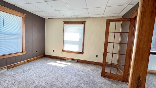 carpeted spare room featuring a drop ceiling, wood walls, and baseboards