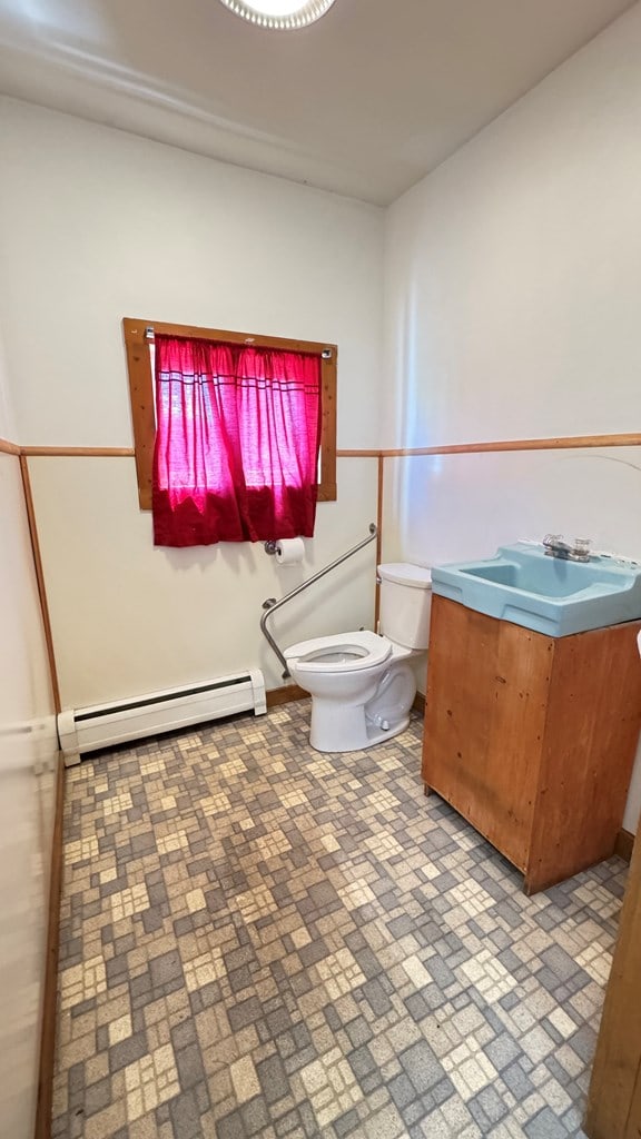 half bathroom featuring baseboard heating, toilet, brick patterned floors, and a sink