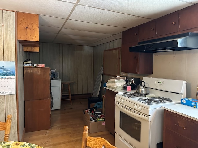 kitchen with light wood-type flooring, a paneled ceiling, white range with gas stovetop, washer / clothes dryer, and wood walls