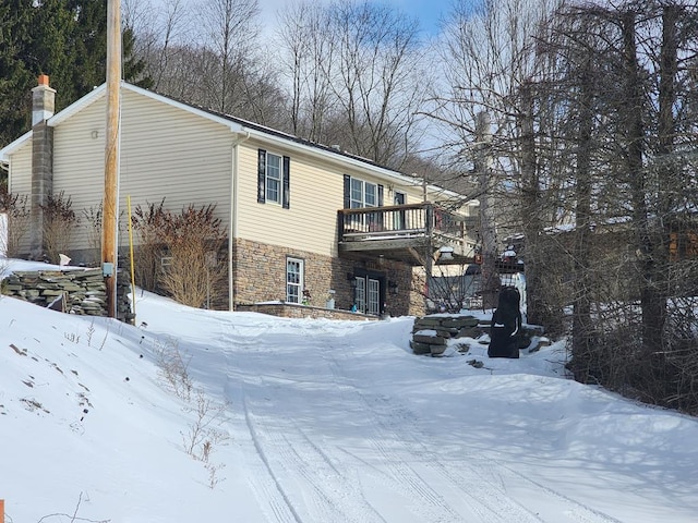 view of snow covered exterior featuring a balcony, stone siding, and a chimney