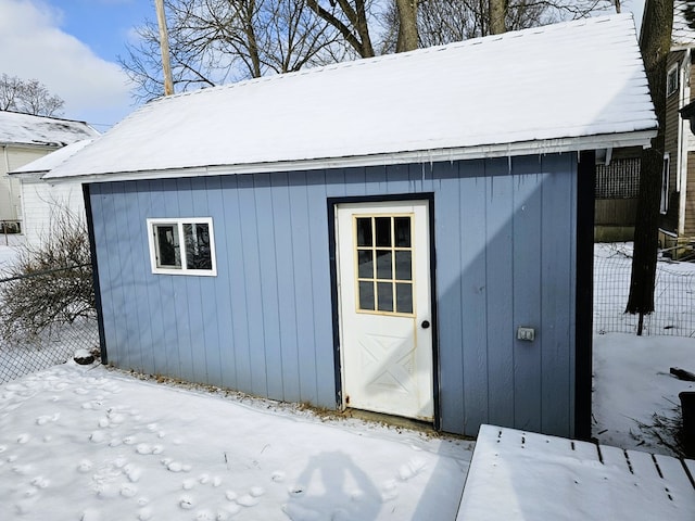 snow covered structure featuring an outbuilding and fence