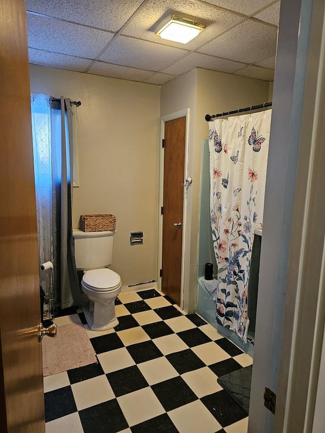 full bathroom with a paneled ceiling, shower / bath combination with curtain, toilet, and tile patterned floors