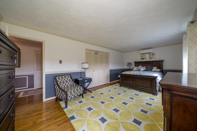 bedroom featuring crown molding, a wall mounted air conditioner, light wood-type flooring, and a closet