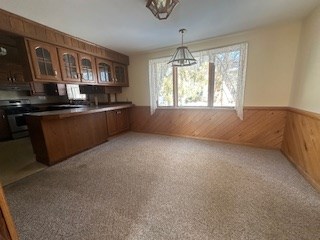 kitchen featuring electric range, carpet flooring, hanging light fixtures, and wood walls