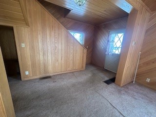 bonus room featuring light carpet, wooden ceiling, and wood walls