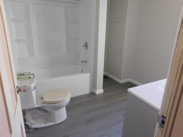 bathroom with baseboards, toilet, shower / bathing tub combination, wood finished floors, and vanity