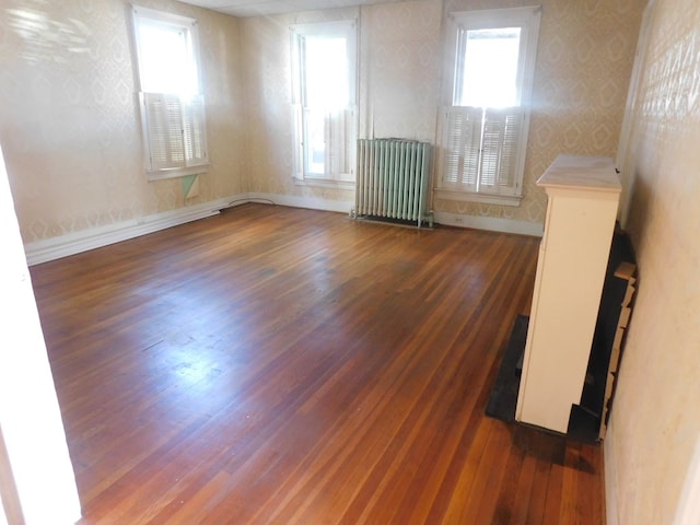 unfurnished room with radiator heating unit, wood finished floors, and baseboards