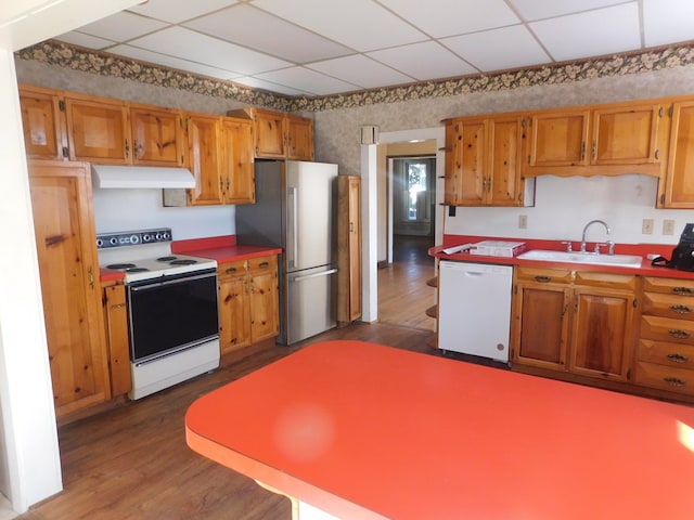 kitchen with under cabinet range hood, white appliances, dark wood-type flooring, and brown cabinetry