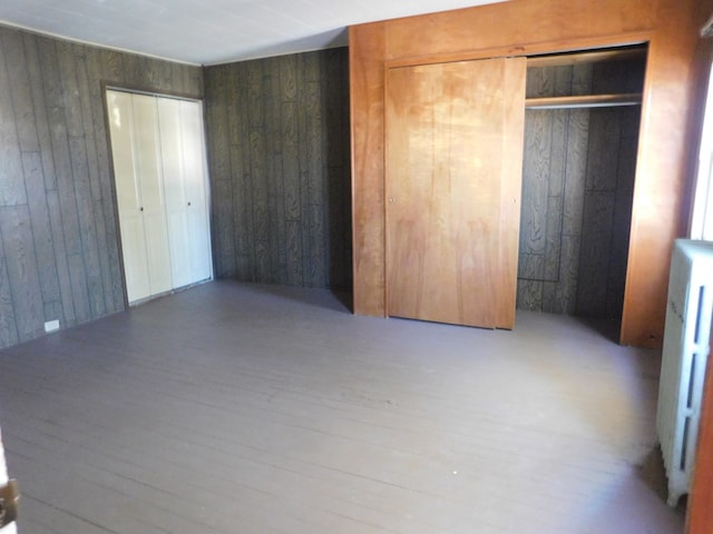 unfurnished bedroom with radiator heating unit, wood finished floors, and wood walls