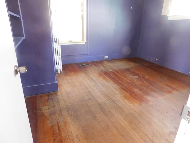 empty room featuring visible vents, radiator heating unit, and hardwood / wood-style flooring