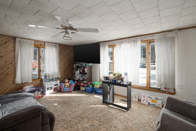 carpeted living room featuring ceiling fan, plenty of natural light, and wood walls