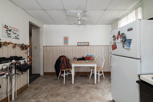 dining space with a drop ceiling, wood walls, and ceiling fan