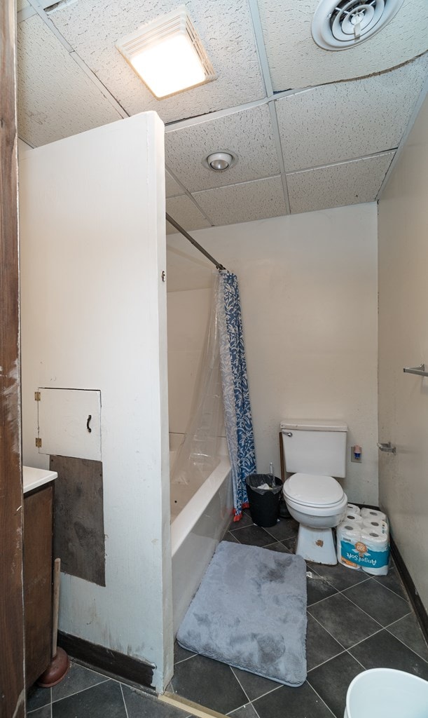 full bathroom with a drop ceiling, tile patterned floors, toilet, shower / tub combo with curtain, and vanity