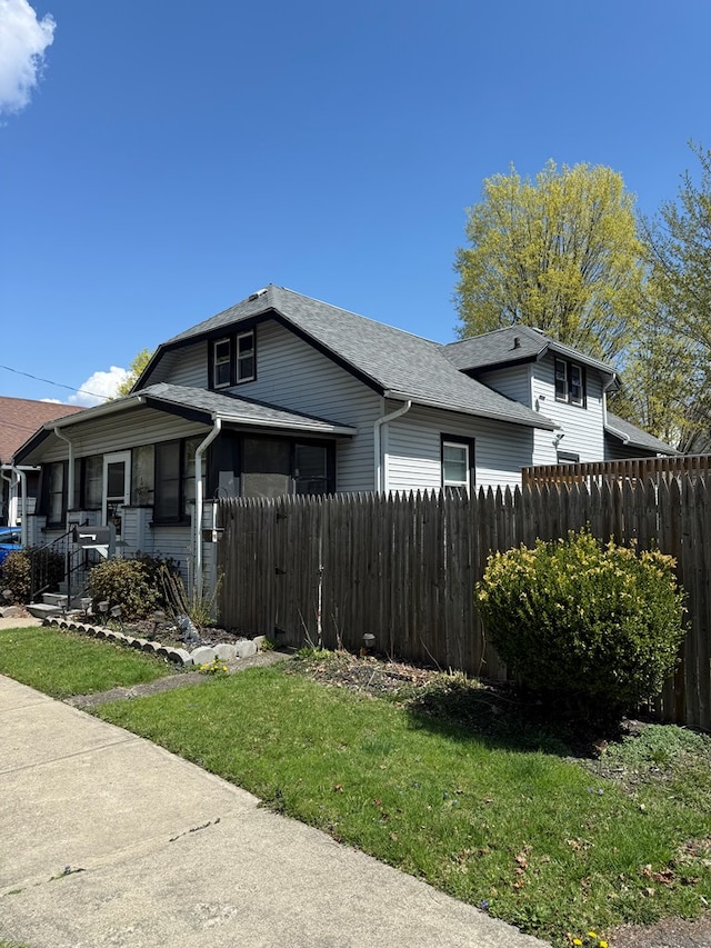 view of side of property with a lawn, a shingled roof, and fence