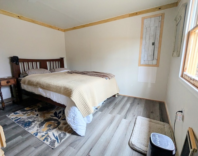 bedroom with wood finished floors, electric panel, and crown molding