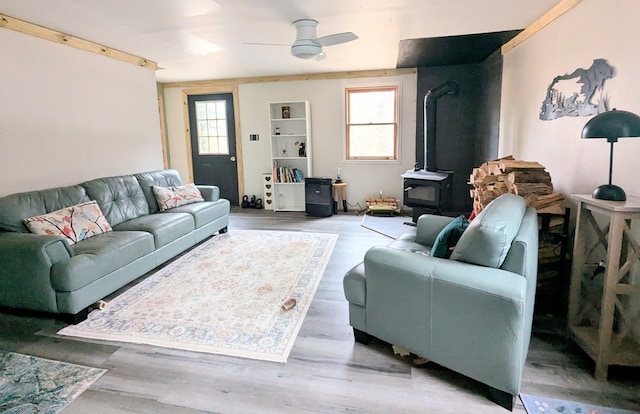 living room featuring a wood stove, a ceiling fan, light wood-style flooring, and a healthy amount of sunlight