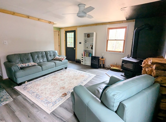 living area with a wood stove, ceiling fan, and wood finished floors