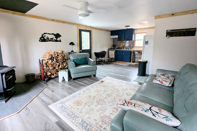 living room featuring light wood-style flooring, a wood stove, and a ceiling fan