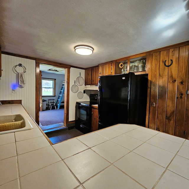 kitchen featuring tile countertops, wooden walls, sink, and black appliances