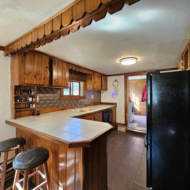 kitchen featuring sink, kitchen peninsula, tile countertops, washer / dryer, and black appliances