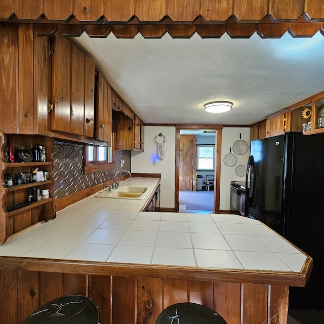 kitchen with tile countertops, black fridge, kitchen peninsula, and sink