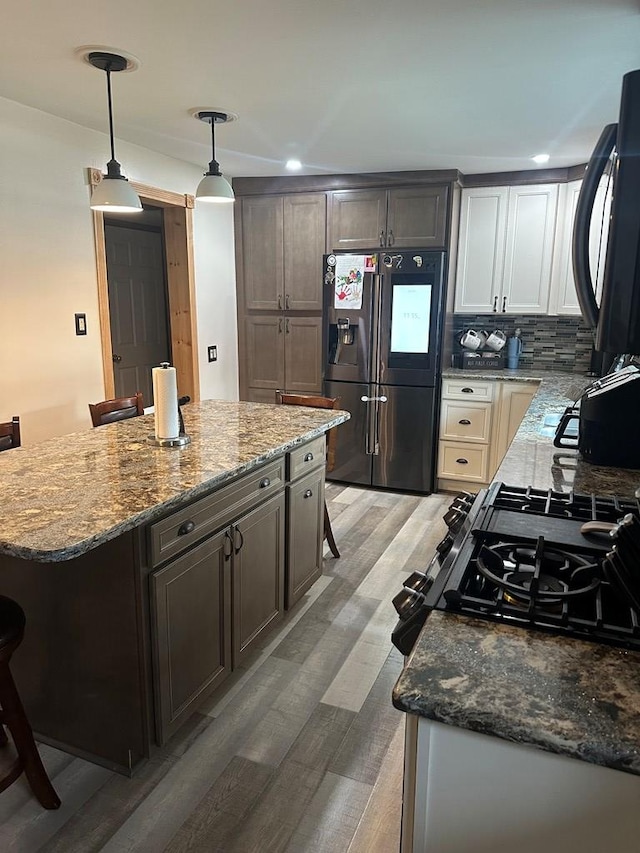 kitchen with a kitchen bar, backsplash, hardwood / wood-style flooring, stainless steel fridge with ice dispenser, and hanging light fixtures