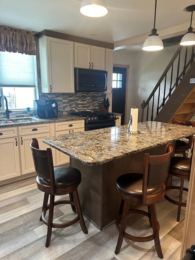 kitchen with a center island, backsplash, black appliances, hanging light fixtures, and a breakfast bar area