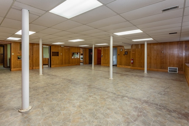 finished below grade area featuring visible vents, a paneled ceiling, and wooden walls